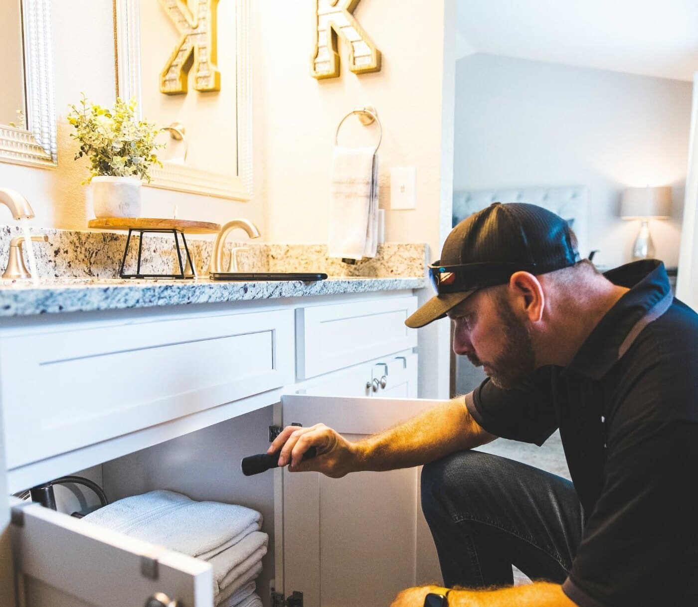 TNT Home Services technician inspecting plumbing under a bathroom vanity